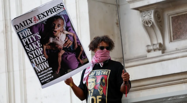 Londra'daki gösteride bir kişi yüksek bir yere çıkmış ve elinde bir çocuğun açlıktan ölüşünü gösteren bir gazete taşıyor.