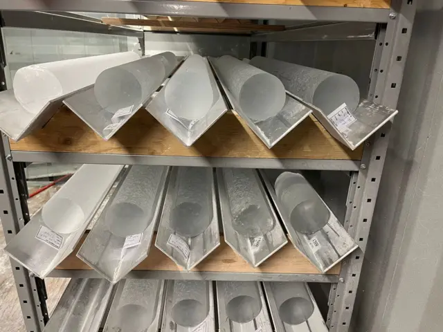 Metal olukların içinde, yaklaşık 15 cm çapında, 15 buz çekirdeği bulunuyor. Bunlar, ahşap ve metal raflara istiflenmiş durumda.