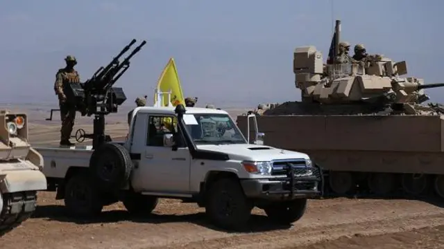 Suriye'nin Haseke bölgesinde bir eğitim sırasında ABD askerleri bir tankta, SDG üyeleri de askeri bir arabanın üzerinde YPG bayrağıyla duruyor.
