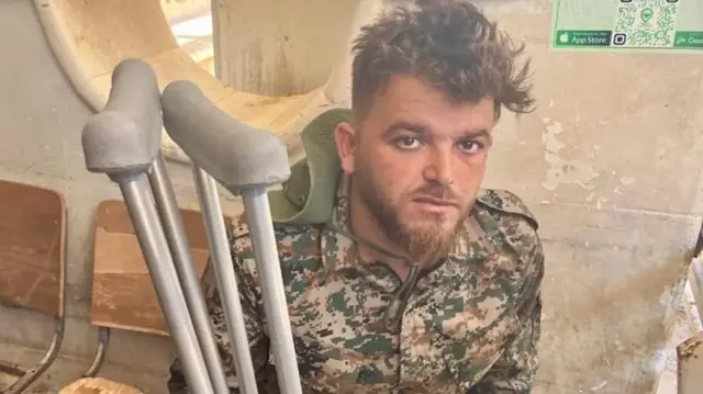 Askeri üniforma giyen bir adam yorgun gözlerle kameraya bakıyor