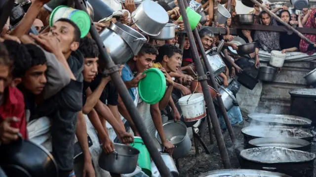 People including young boys wait in line to receive hot meals distributed by GHF in Gaza City